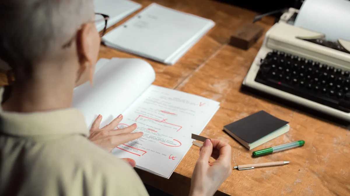 AI content governance and editorial control — The Complete Guide Editor reviewing marked-up pages at a desk with writing tools