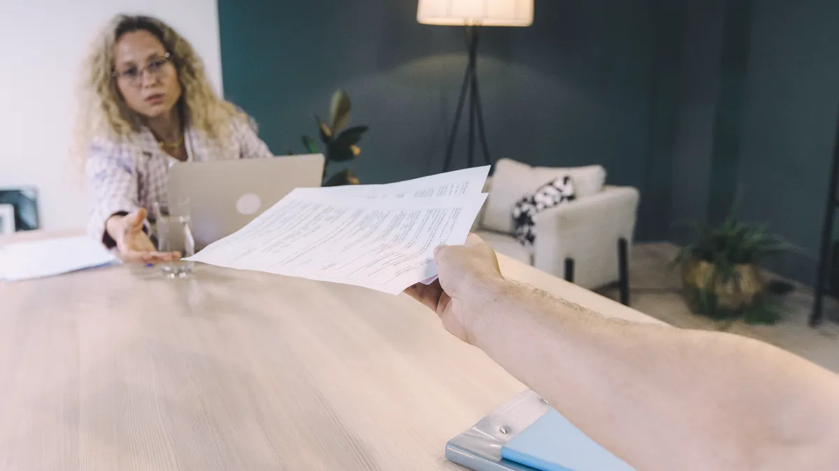 document being handed across a table to a person at laptop