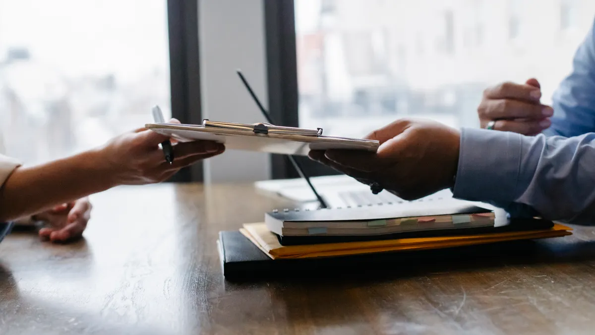 hands passing a folder across a desk