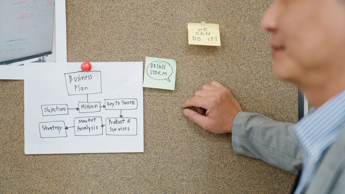 Person arranging notes on a corkboard flowchart